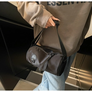 Close-up of a black nylon cylinder crossbody bag with a round logo and adjustable strap
