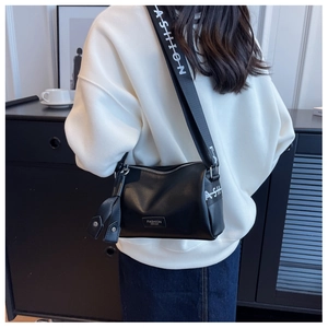 Détail d'un sac à main noir en cuir grainé avec une large bandoulière lettrée