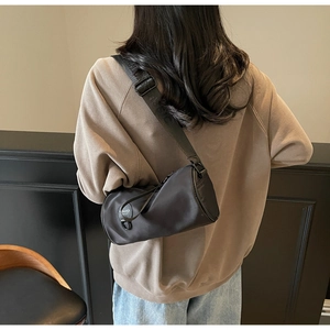 Close-up of black cylinder crossbody bag showing the adjustable wide woven strap and side logo