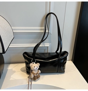 Detail of black patent leather shoulder bag with glossy finish and cute teddy bear charm
