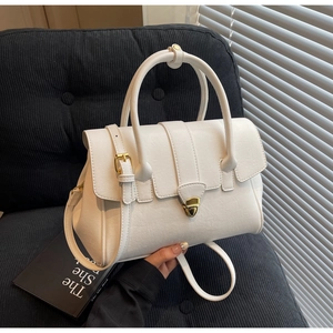 Weiße Handtasche aus Kunstleder mit goldenem Drehverschluss auf einem dunklen Sessel