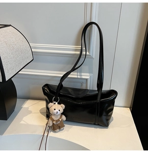 Detail of black patent leather shoulder bag with teddy bear charm on white table