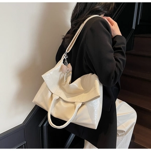 Detail of a creamy white tote bag with a plaid bow pendant worn by a model