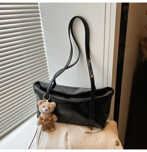 Detail of black glossy faux leather tote bag with a cute plush bear charm accessory