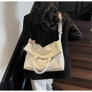Detail of cream white faux leather tote bag with elegant pearl and bow charm on a model