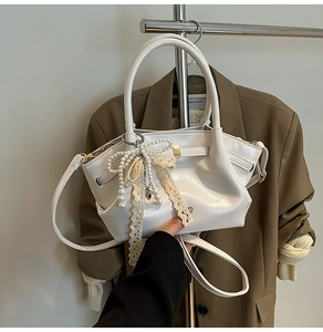 Detail der cremefarbenen Glanzhandtasche mit Perlenbogen Spitze und Herz-Anhänger