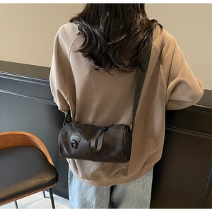 Detail of a black cylindrical crossbody bag with a wide branded shoulder strap