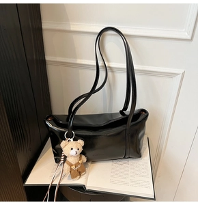 Detail of minimalist black shoulder bag featuring a plush bear charm on a magazine