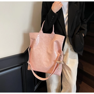 Detail of pink glossy leather tote bag with stylish bow charm and adjustable strap