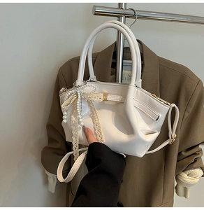 Detail der weißen PU-Ledertasche mit Schleife und Perlenanhänger vor Anzug-Hintergrund