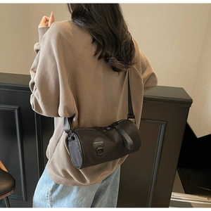 Detail of a black nylon cylinder crossbody bag worn by a model in a lifestyle setting