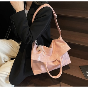 Close-up of pink glossy tote bag with pearl bow charm on a model in black suit