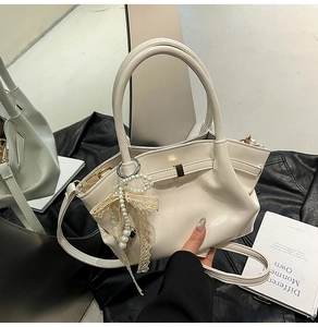 Makro-Detail der cremeweißen Leder-Eimertasche mit Perlen und Spitzen-Anhängern