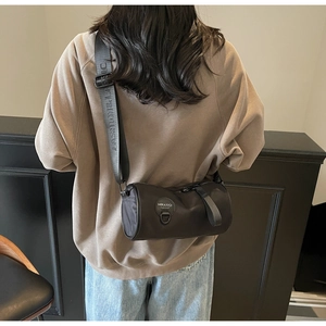 Close-up of black cylinder crossbody bag with branded strap worn by model