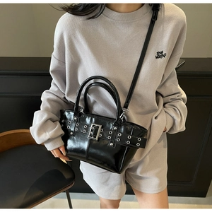 Dettaglio borsa tote in pelle nera lucida con fibbie punk su outfit grigio