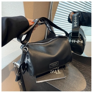 Détail du sac cylindre en cuir noir grainé avec large bandoulière et logo moderne