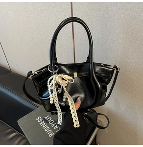 Detail der schwarzen glänzenden Lederhandtasche mit Perlen- und Spitzenanhänger