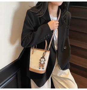 Détail d'un sac seau chic avec charme de poupée, porté par un mannequin en décor minimaliste