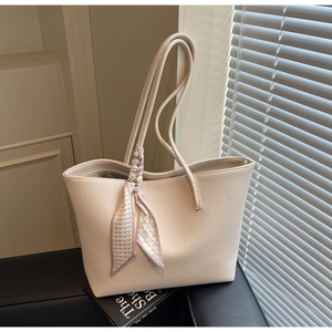Detail of beige tote bag featuring litchi texture and decorative silk scarf on strap