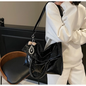 Detail of glossy black leather tote bag with pearl bow charm and dual handle straps
