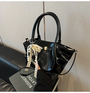 Detail einer schwarzen glänzenden PU-Lederhandtasche mit Perlen- und Spitzenanhänger
