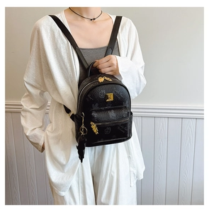 Detail of black faux leather mini backpack with golden logo and cute bear pendant