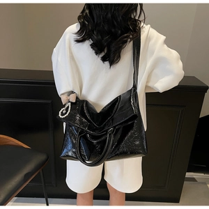 Close-up of black glossy tote bag with plaid bow and pearl pendant on model