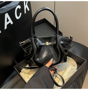 Detail der schwarzen Handtasche aus Faltenleder mit goldener Schnalle und Rundgriffen
