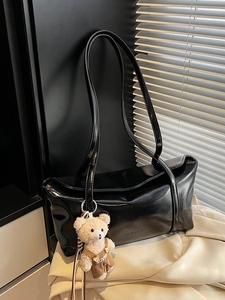 Minimalist black leather shoulder bag with plush bear charm and glossy finish