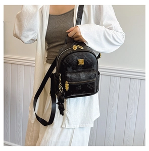 Close-up of black lychee grain leather backpack featuring a golden bear charm and logo