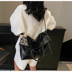 Detailed view of black tote bag with glossy wrinkled texture and pearl bow charm detail