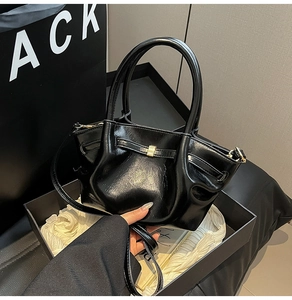 Detail einer schwarzen glänzenden Handtasche mit goldener Schnalle und Zierriemen