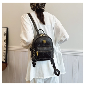 Close-up of black backpack with teddy bear print and plush charm on a model
