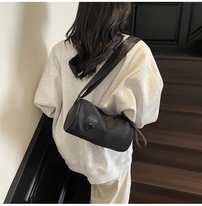 Detail of black oxford cylinder crossbody bag with embroidered strap on a grey hoodie