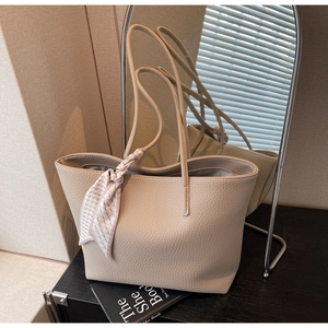Close-up of beige litchi grain tote bag with decorative scarf on a wooden surface