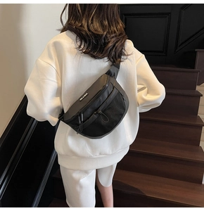 Détail d'un sac bandoulière noir en nylon avec sangle réglable porté sur un sweat à capuche blanc