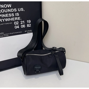 Detail of minimalist black nylon cylinder bag with metal zipper and wide woven strap