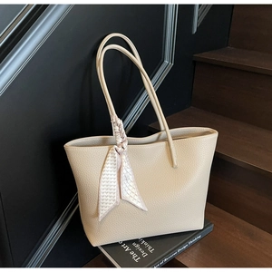Detail of beige tote bag with lychee texture and decorative scarf on wooden stairs