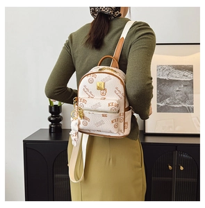 Detail of cream mini backpack featuring collegiate logo print and a cute bear charm
