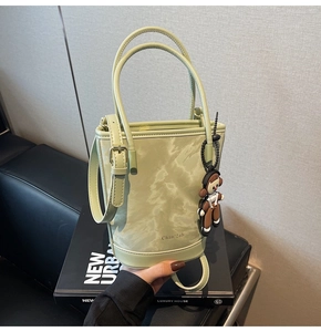 Détail d'un sac seau vert clair à motif marbré avec charm poupée et bandoulière fine