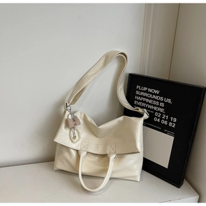 Close-up of beige patent leather tote bag with pleated texture and pearl bow charm