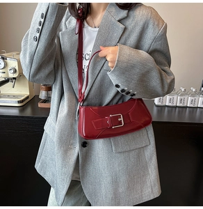 Close-up of a red patent leather underarm bag with silver buckle on a gray blazer