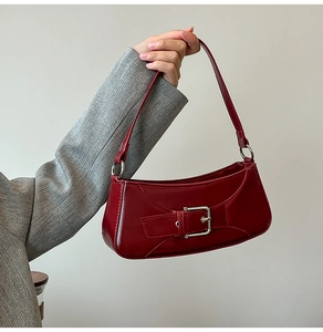 Close-up of bright red glossy leather baguette bag with oversized silver metal buckle