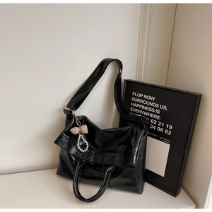 Detail of black glossy tote bag with plaid bow and pearl pendant decoration