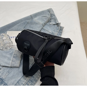 Detail of black cylindrical crossbody bag with wide logo strap and silver zipper hardware