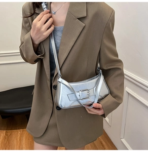 Close-up of a silver metallic underarm bag with a wide buckle detail on a model