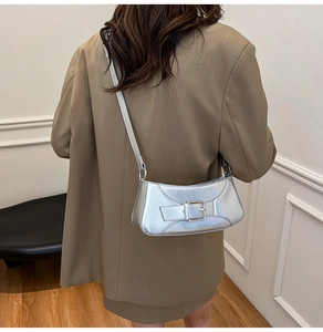 Close-up of metallic silver baguette bag with buckle detail on a model in a brown blazer
