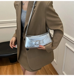 Detail view of a silver metallic baguette bag with large buckle strap on a model