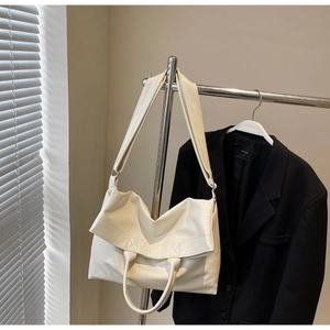 Close-up of cream white glossy leather tote bag with long strap and top handle design