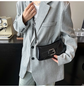 Detail of a black glossy baguette bag with silver buckle worn over a grey blazer